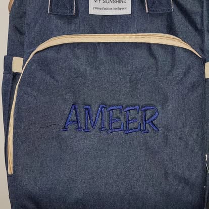 Navy denim backpack with the name 'Ameer' embroidered in blue block letters.