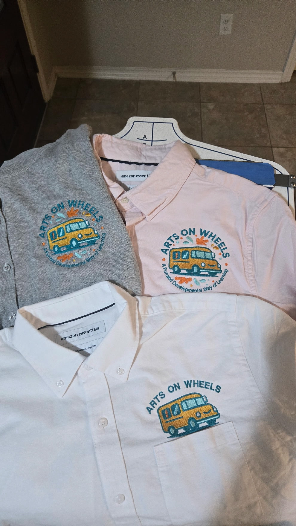 Three button-down shirts embroidered with the Arts on Wheels school-bus logo.