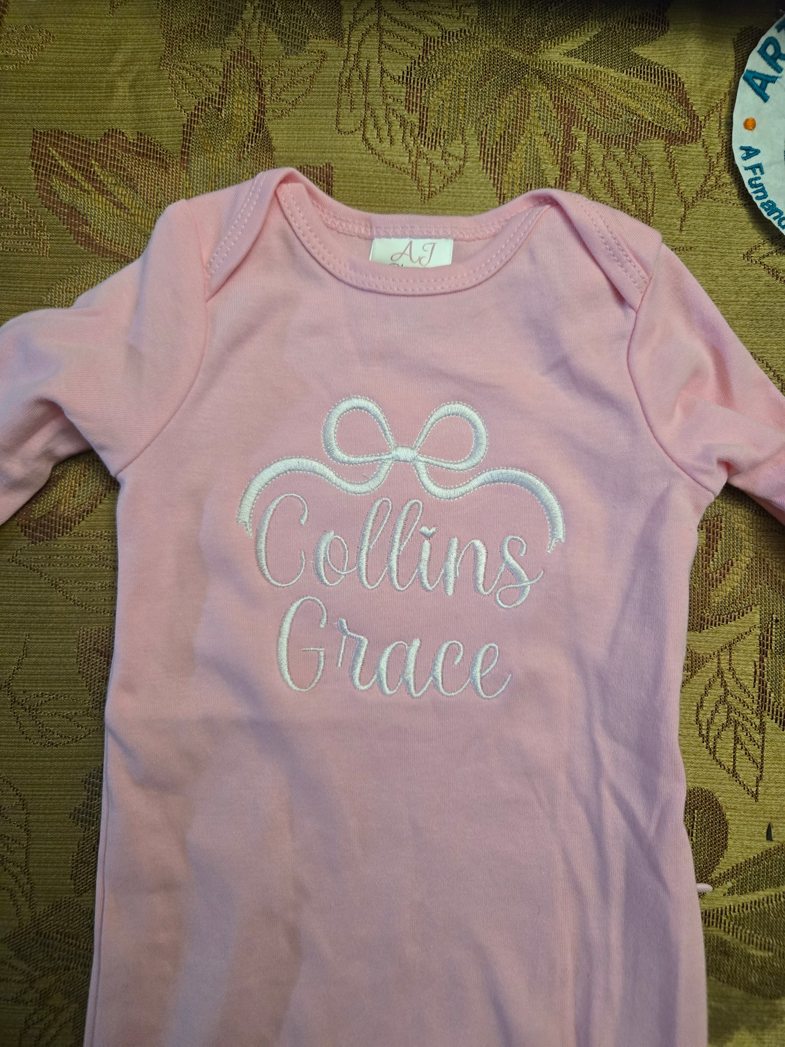 Pink baby gown with a white embroidered bow and the 'Collins Grace' monogram.