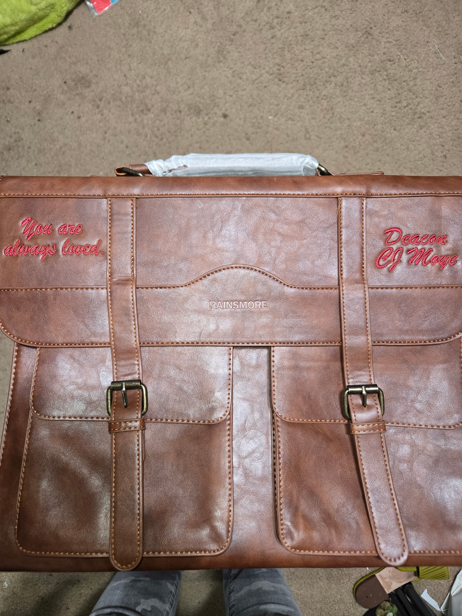 Brown satchel embroidered with 'You are always loved.' and 'Deacon CJ Moye' in script.