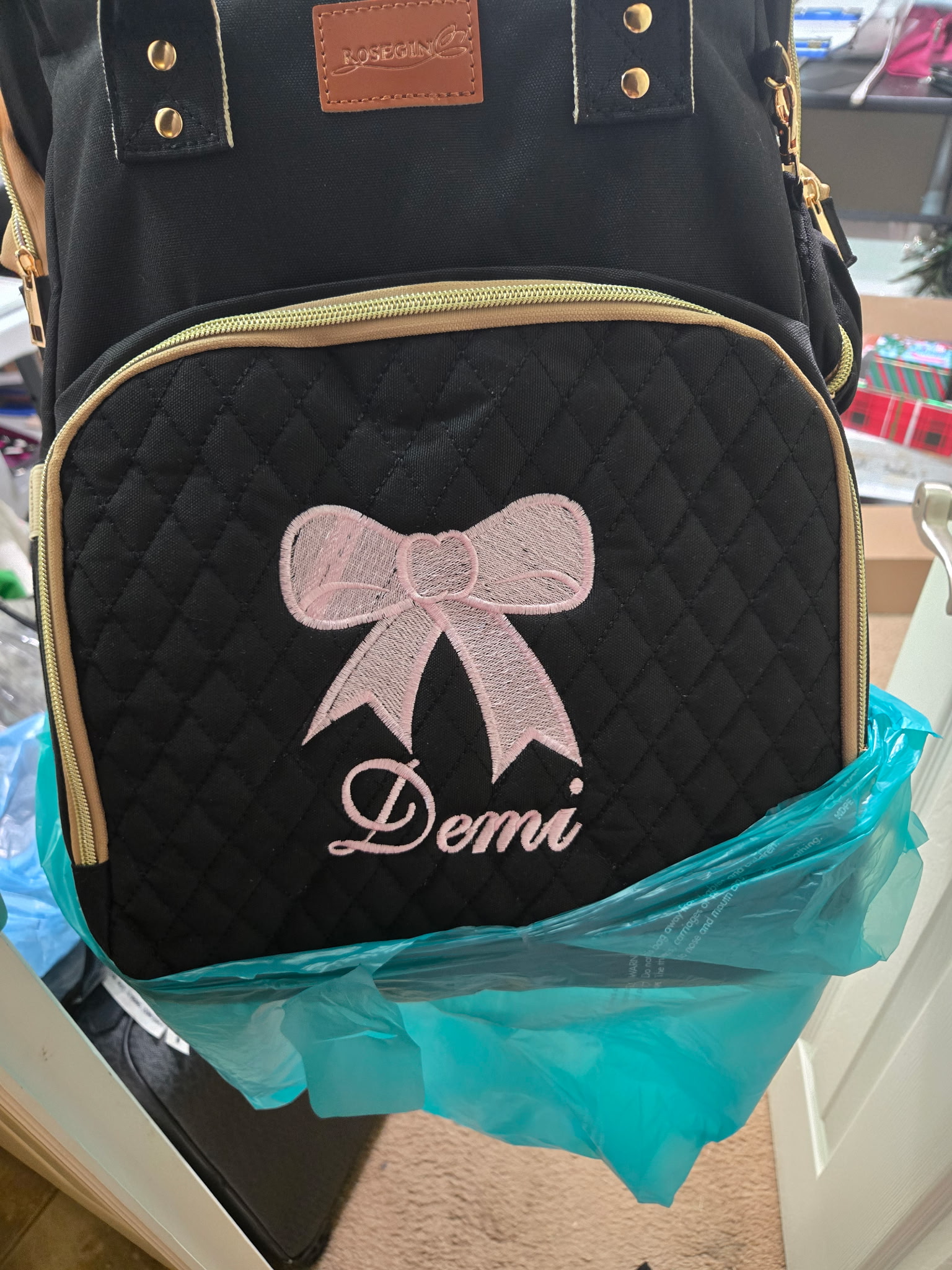 Black quilted backpack with a pink embroidered bow and the name 'Demi' in script.