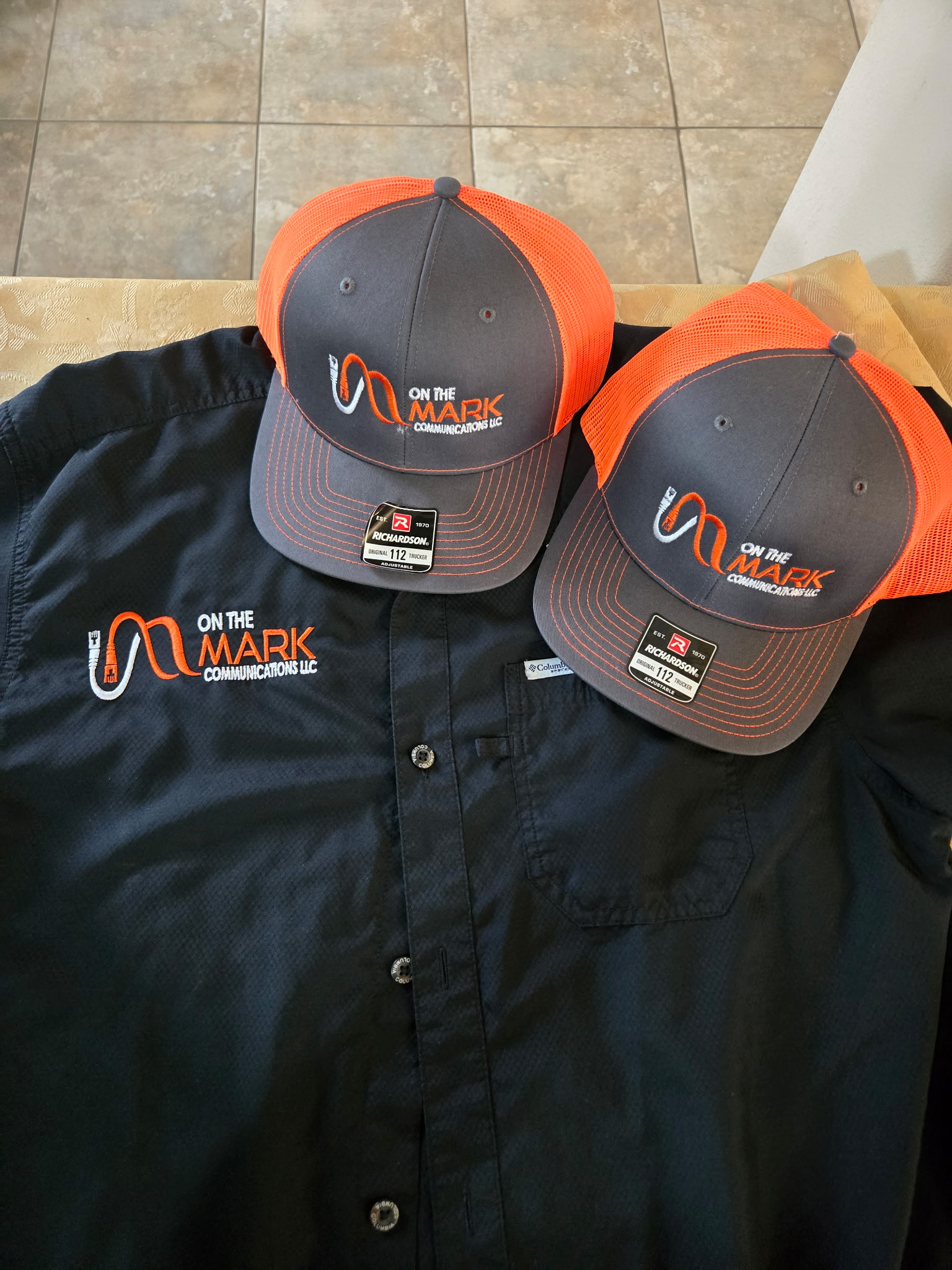 Orange and charcoal trucker caps and a work shirt embroidered with the On The Mark Communications logo.